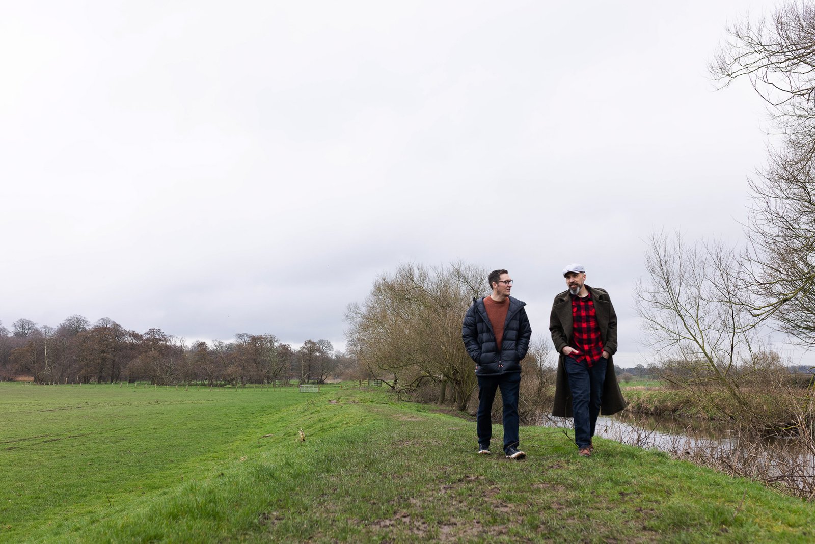 James and Garry walking along a riverbank under a wide sky