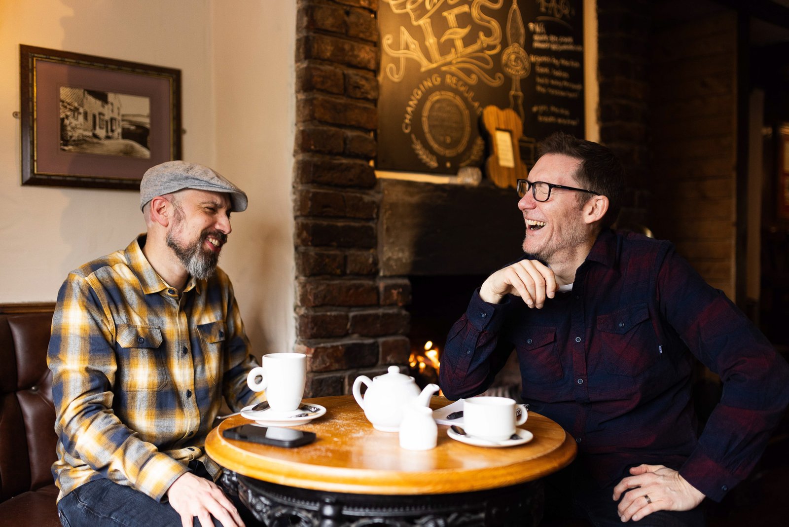 James and Garry laughing over tea by a pub fire
